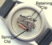Watch battery retained by a spring clip watch